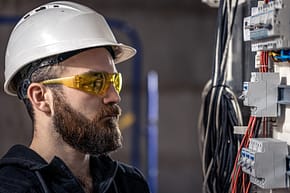 A male electrician works in a switchboard with an electrical connecting cable. A male electrician works in a switchboard with an electrical connecting cable, connects the equipment with tools.