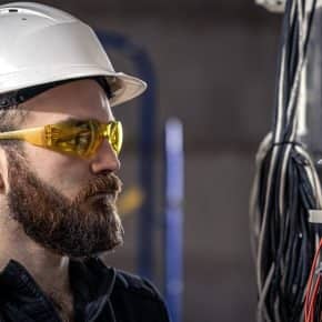 A male electrician works in a switchboard with an electrical connecting cable. A male electrician works in a switchboard with an electrical connecting cable, connects the equipment with tools.